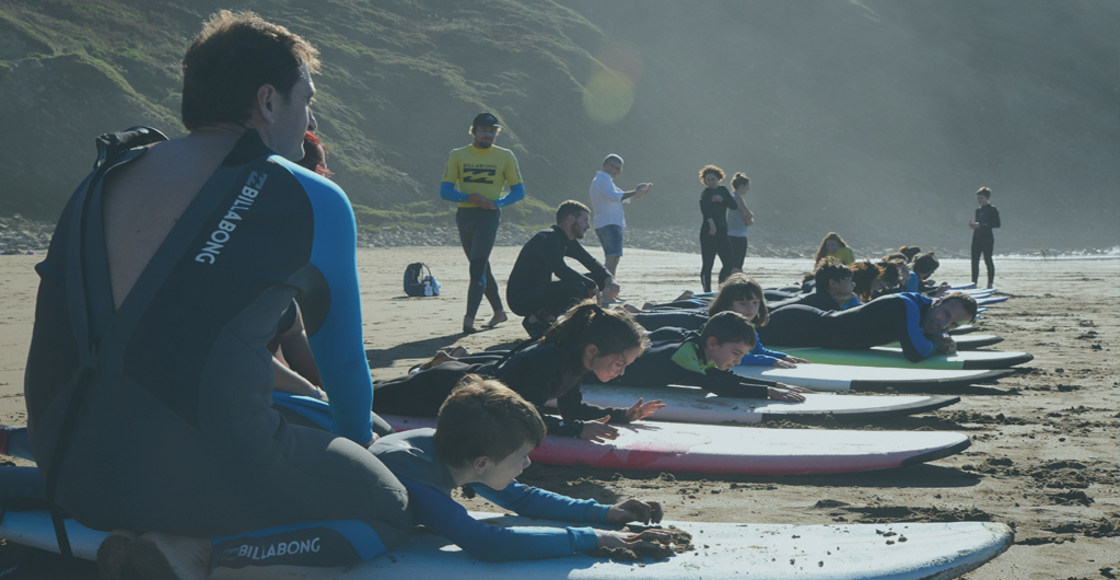 NIñas y niños aprenden a hacer surf tumbados en sus tablas encima de la arena
